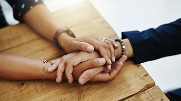 Hands holding abuse victim in a therapy session for support and comfort by a professional psychologist