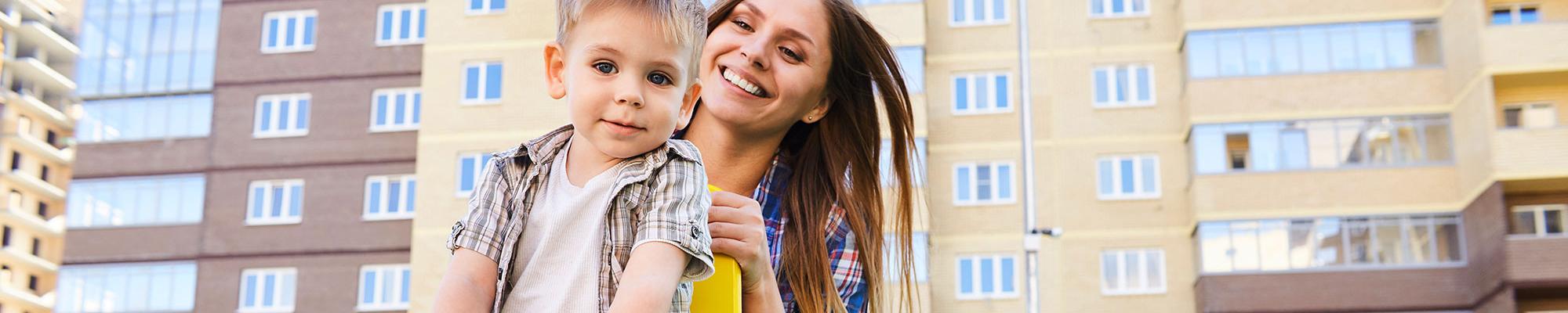 Portrait of young mother playing with son in front of apartment building.