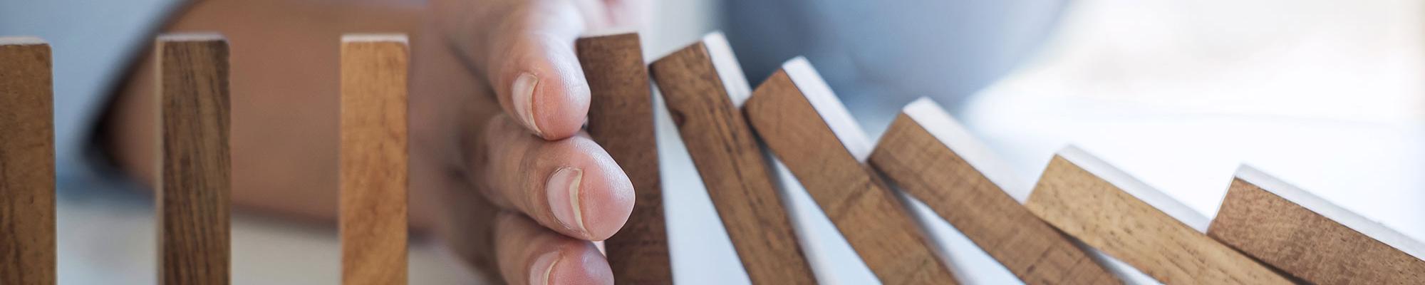 Risk and Strategy in Business, Image of hand stopping falling collapse wooden block dominoes effect from continuous toppled block, prevention and development